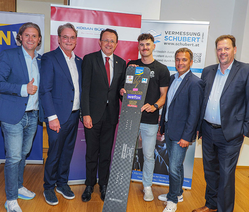 Gruppenfoto mit 6 Personen in Anzug, ein junger Mann in Sportkleidung hält sein Snowboard