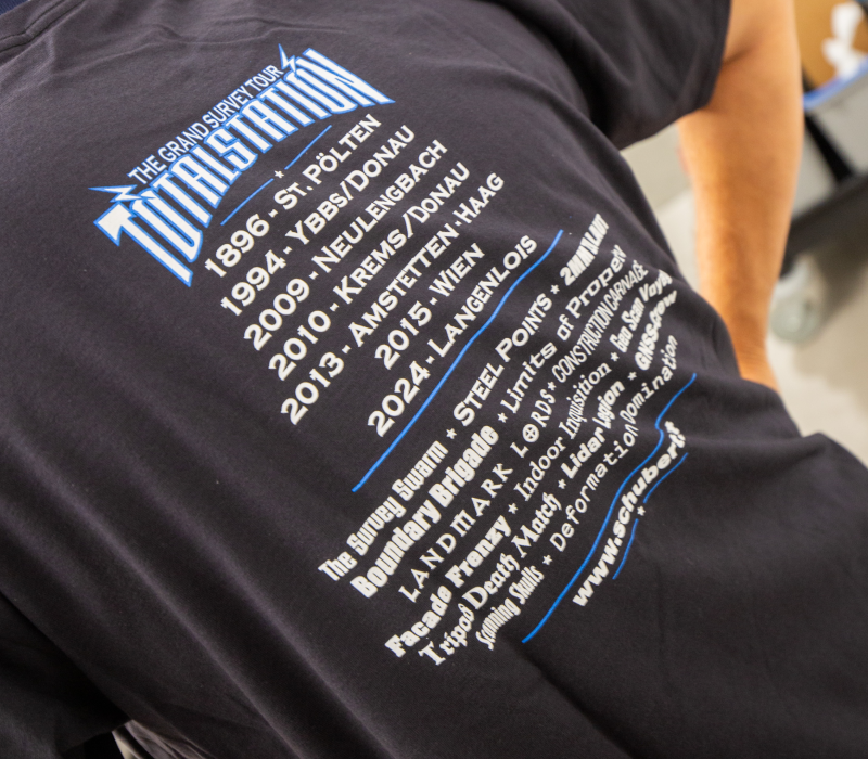 Mitarbeiter zeigt die R&uuml;ckseite eines schwarzen T-Shirts im Rockfestival-Stil