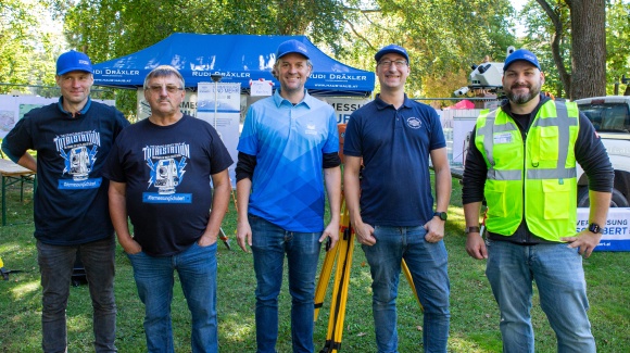 5 m&auml;nnliche Personen in Firmen-T-Shirts stehen vor einem aufgebauten Stand