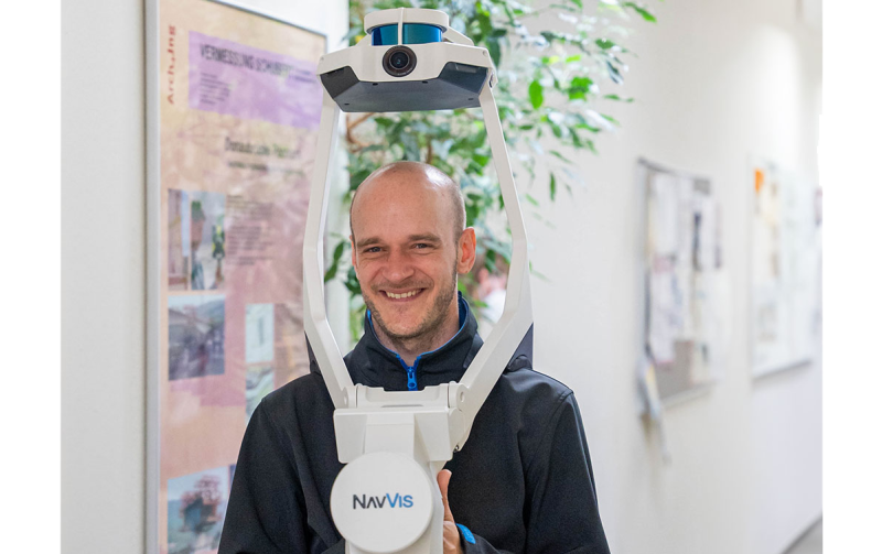 Ein Mann tr&auml;gt einen mobilen Laserscanner und vermisst einen Flur, Blick in die Kamera